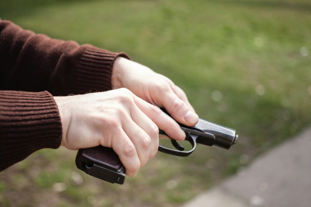 A man charges a gun against a green grass. Firearms gun outdoor. Sport, hobbies