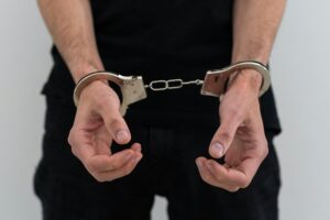 arrested man with cuffed hands behind prison bars.