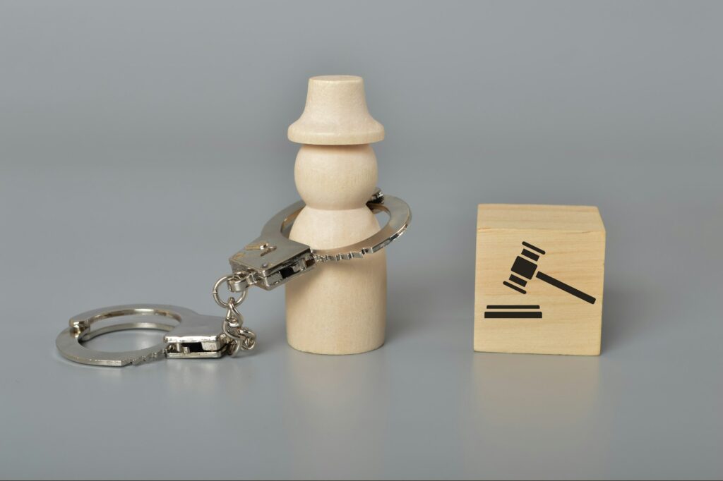 Arrested wooden people with handcuffs and judge gavel symbol.