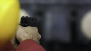 Back view of man shoots a gun at shooting range close up. Man fires hand gun at indoor shooting