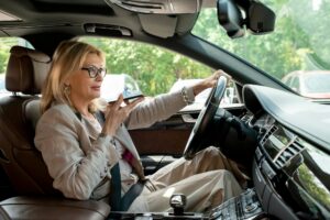 Blond elegant mature businesswoman recording voice message while driving