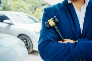 businessman in a suit and a lawyer, holding a wooden gavel, stand in front of a car
