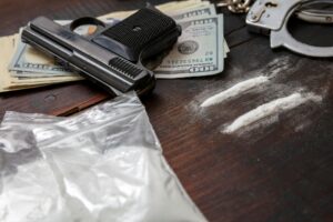 Drugs smuggling and trafficking, Handcuffs, pistol money and cocaine on wooden table background