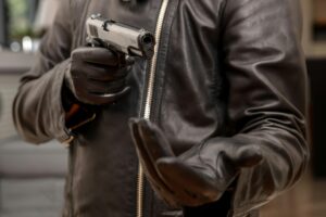 Gloved hand holding a pistol aiming, closeup view. Armed robbery concept