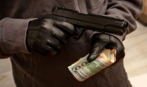 Gloved hand holding a pistol stealing money, closeup view. Armed robbery concept