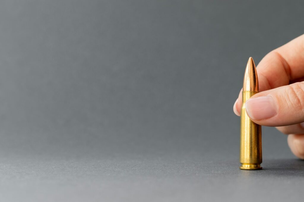 Hand with bullet on gray background. Cartridge 7.62 caliber for Kalashnikov assault rifle