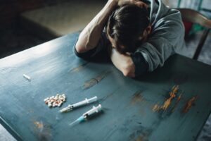 Male junkie at the table with drugs and syringe