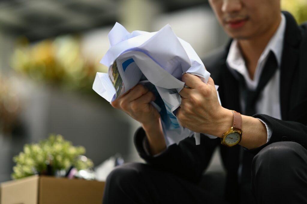 Dismissed businessman crumpling papers, stress from losing job.