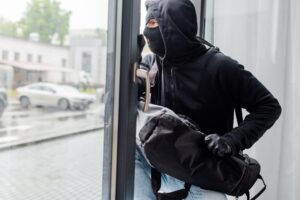 Robber in balaclava and leather gloves holding bag near open window