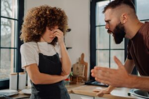 Couple arguing in kitchen, frustrated woman listening to man shouting