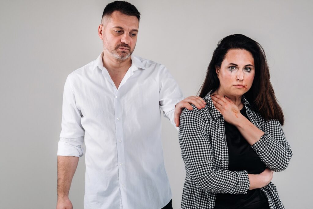 A woman beaten by her husband standing behind her and looking at her aggressively. Domestic violence