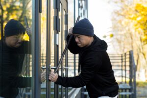 Asian man robber tries to break the door lock with a large metal crowbar tool