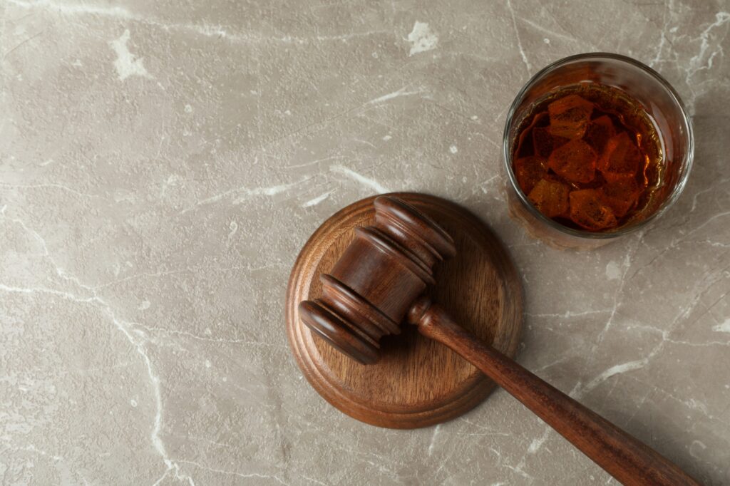 Judge gavel and glass of whiskey on gray textured table