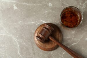 Judge gavel and glass of whiskey on gray textured table