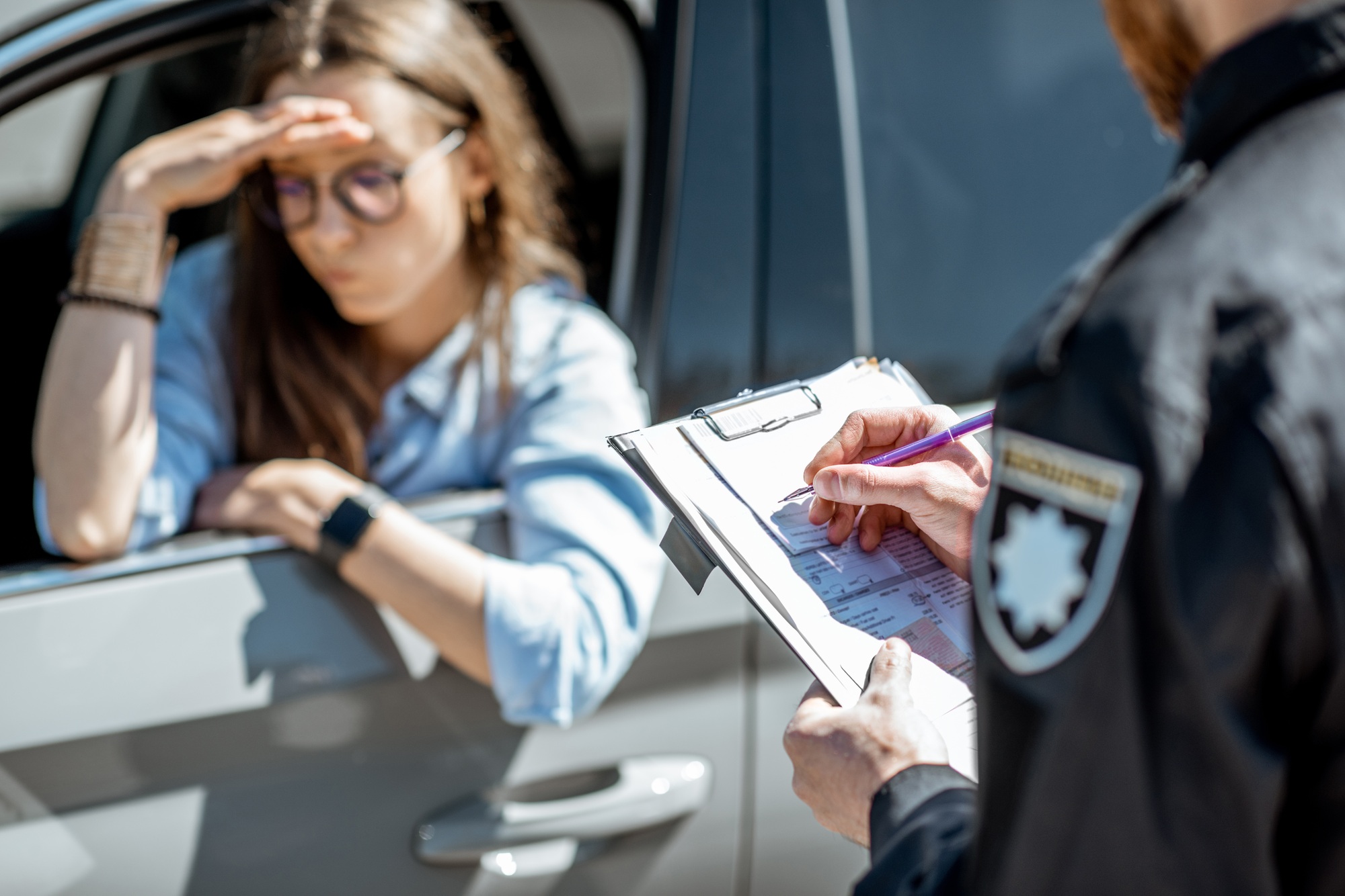 Policeman issuing a traffic fine to a female driver looking distressed, emphasizing legal consequences related to suspended licenses and the importance of defense lawyers in such situations.