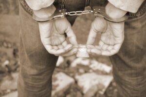 Arrested drug dealer in police handcuffs with small heroin drug