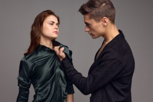 A man holds a woman by the collar on a gray background aggression distrust