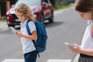 Blonde boy with a backpack, and cellphone goes through the pedestrian crossing
