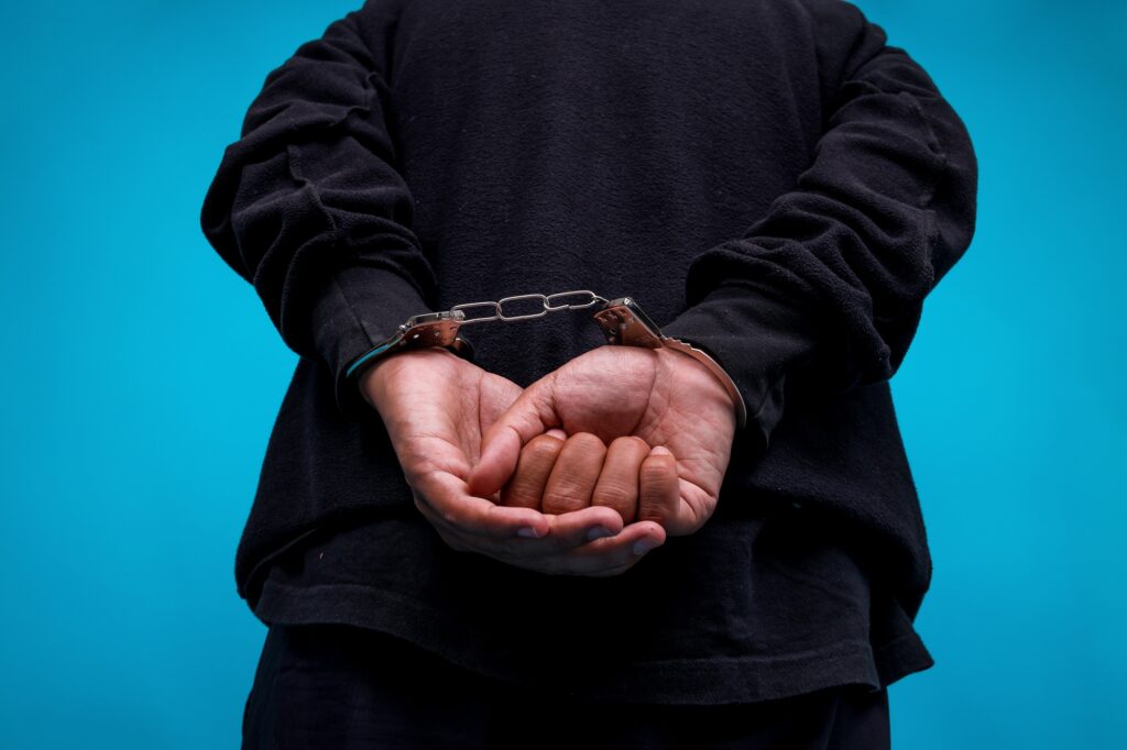 Close-up Of Hands Arrested With Handcuffed In Back Isolated On Blue Background
