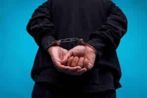 Close-up Of Hands Arrested With Handcuffed In Back Isolated On Blue Background