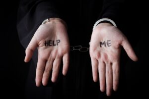 Woman Wearing Handcuff With Help Me Word On Her Palm Against Dark Background