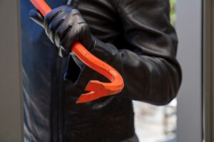 Burglar holding a crowbar to break a glass window.