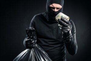 Man in balaclava holding plastic bag with cash and dollars