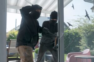 Two burglars opening terrace door of an one-family house with hammer and crowbar at daytime