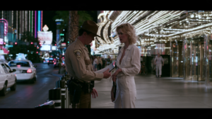 Law enforcement officer speaking with a woman on the Las Vegas Strip during a nighttime vice-related investigation.